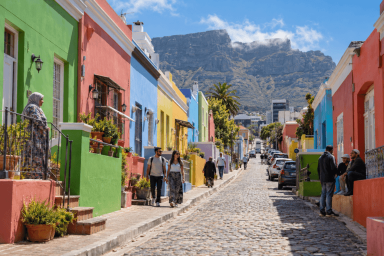 Photorealistic daytime view of a cobbled Bo-Kaap street with colourful Cape Malay houses, pedestrians and Table Mountain in Cape Town