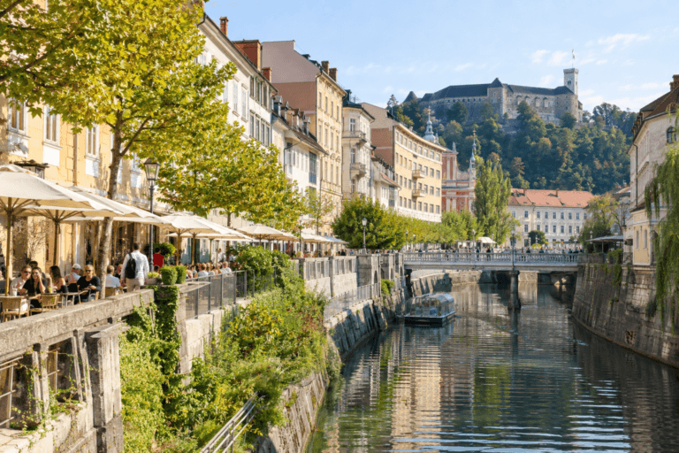 Photorealistic view of Ljubljana riverside near the Triple Bridge, with pedestrians, cafés and the castle in the distance