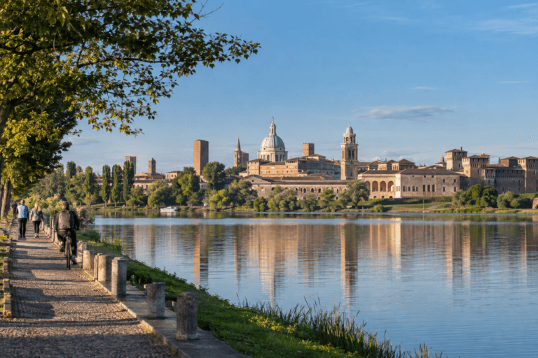 Photorealistic morning view of Mantua's historic skyline across Lago di Mezzo with walkers and a cyclist on the lakeside path