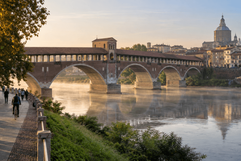 Photorealistic morning view of Pavia's Ponte Coperto over the Ticino River with light mist, walkers, a cyclist and the city skyline