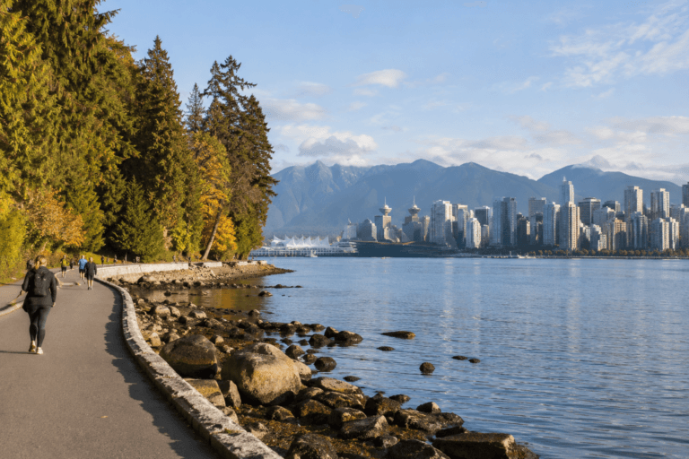 Photorealistic view of walkers on the Vancouver Seawall beside Stanley Park, with the downtown skyline and North Shore mountains